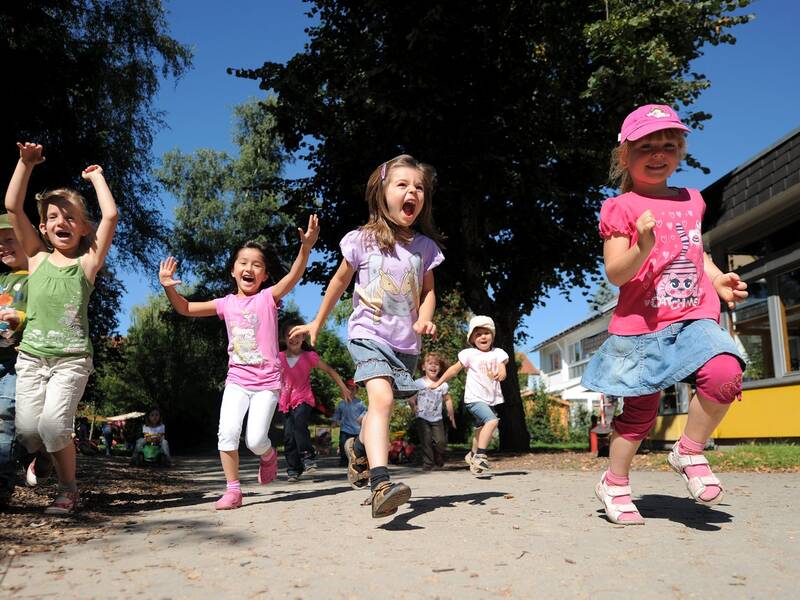 Eine Gruppe von fröhlichen Kindern rennt lachend über einen von Bäumen gesäumten Weg.