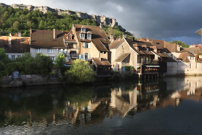 Eine Kulisse mit Reihen von Häusern liegt am Ufer eines Flusses von Ornans.