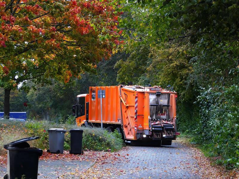 Orangenes Müllauto sammelt Müll aus Mülltonnen ein.