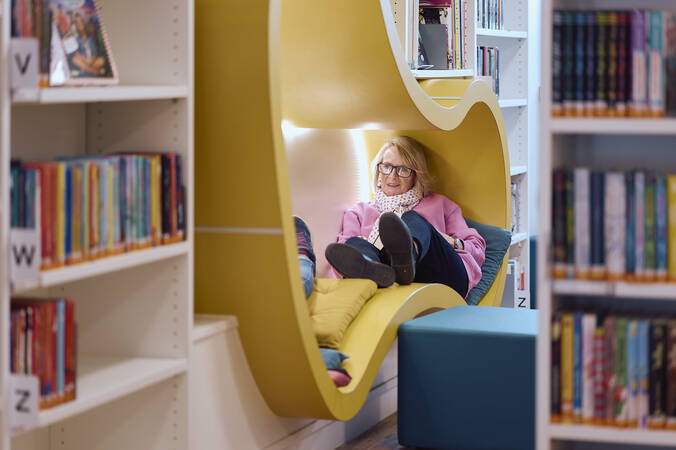 Frau Constanze Amort liest einem Kind, das in einer gelben Leseecke in der Kinder- und Jugendbibliothek Hüfingen sitzt, ein Buch vor.