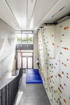 Eine Person klettert an einer bunten Indoor-Kletterwand, die sich in dem modernen, lichtdurchfluteten Flur der Lucian-Reich-Schule mit Treppe und blauen Sicherheitsmatten befindet.