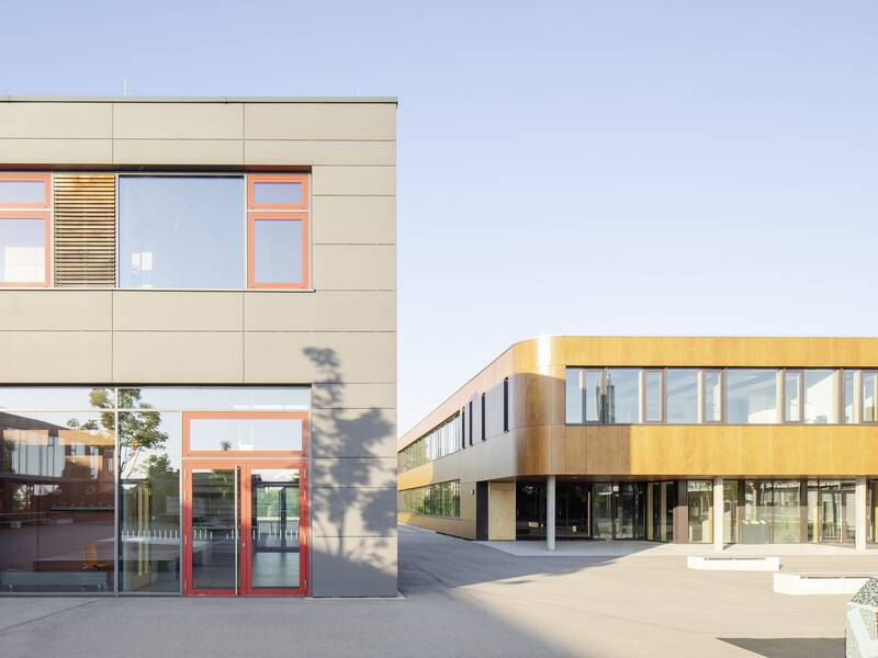 Das Bild zeigt einen den modernen Gebäudekomplex der Lucian-Reich-Schule mit großen Fenstern und einem flachen, eckigen Design in neutralen Farben.