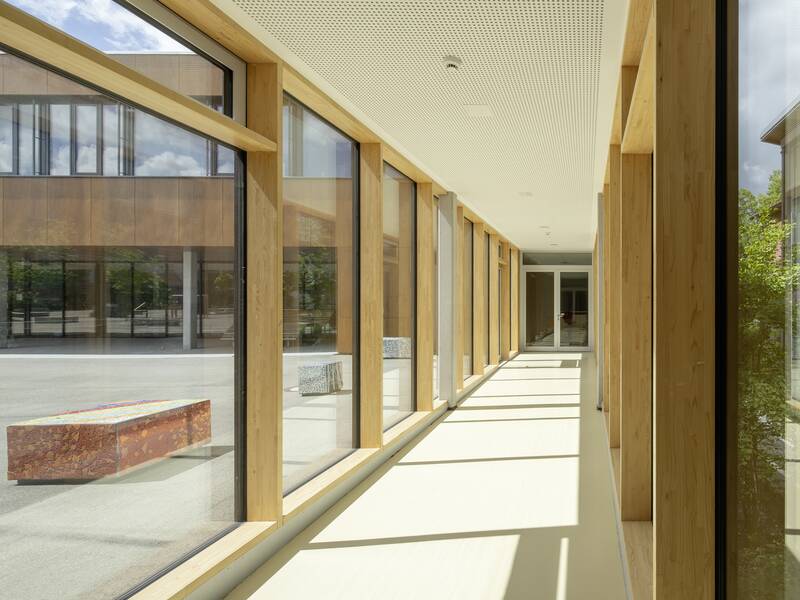 Der helle Flur in der Lucian-Reich-Schule mit großen Fenstern auf der rechten Seite, bietet Ausblick auf den Schulhof mit modernen Sitzgelegenheiten.