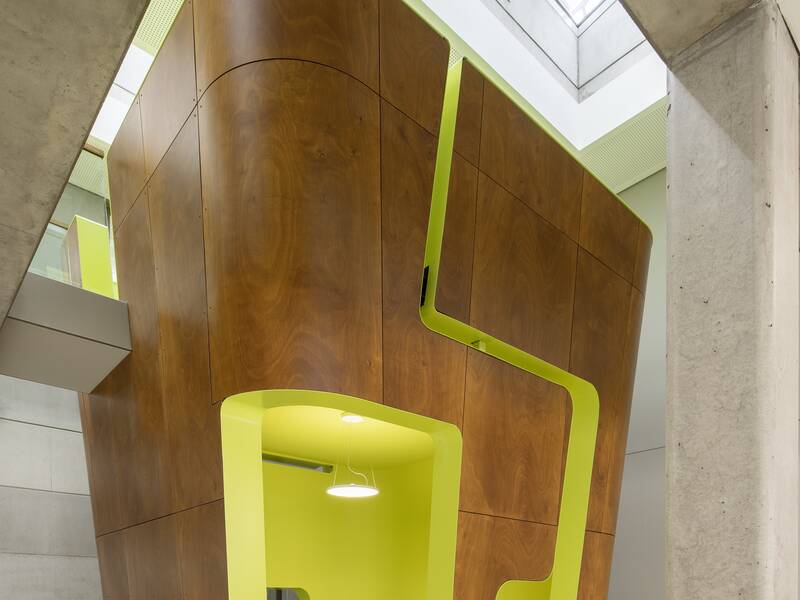 Ein modernes Interieur mit einer Kombination aus glänzenden Holz- und leuchtend gelben Wänden, darunter ein Sitzbereich mit Tisch und Stühlen sowie von oben einfallendem Tageslicht.