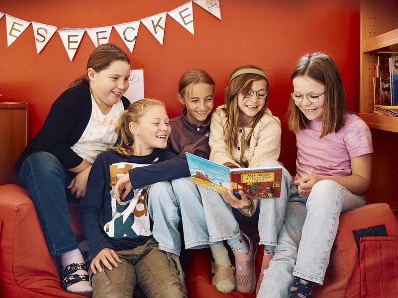 Fünf Kinder sitzen in einer gemütlichen Leseecke in der Schellenberger Schule und lesen gemeinsam ein Buch.