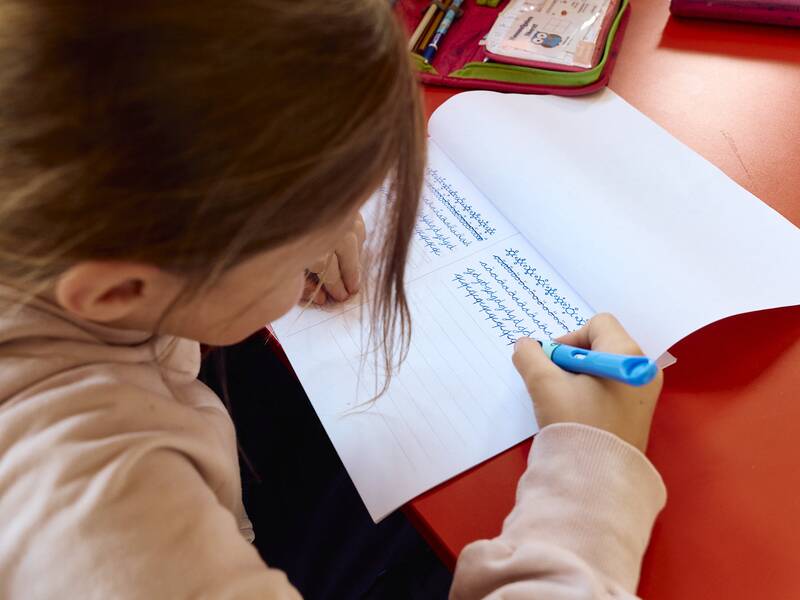 Ein Kind sitzt an einem Tisch im Flur der Schellenberger Schule und schreibt mit einem blauen Stift in ein liniertes Heft.