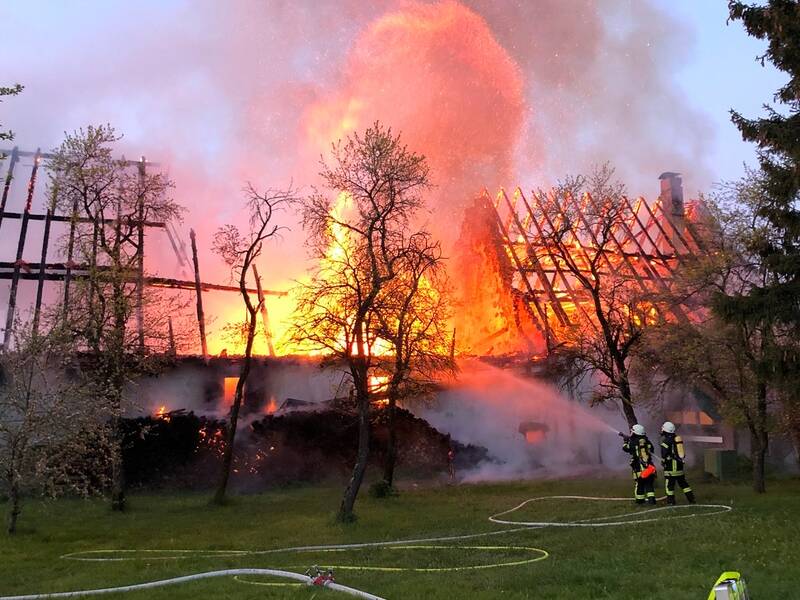 Zwei Feuerwehrmitglieder löschen ein brennendes Gebäude.
