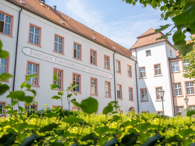 Das historisches Gebäude mit der Aufschrift "Fürstlich Fürstenbergisches Altenpflegeheim" ist von grünen Büschen und Bäumen umgeben.
