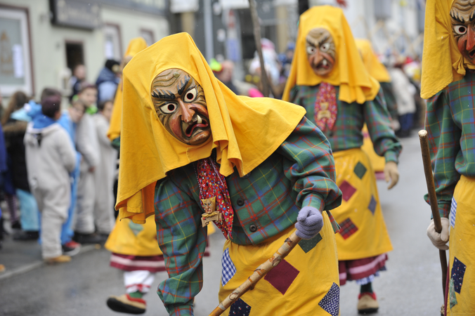 Narrenfigur "Berghexe" trägt eine Hexenlarve mit gelben Tuch, grün karriertes Oberteil und gelbe Schürze mit bunten Flecken 