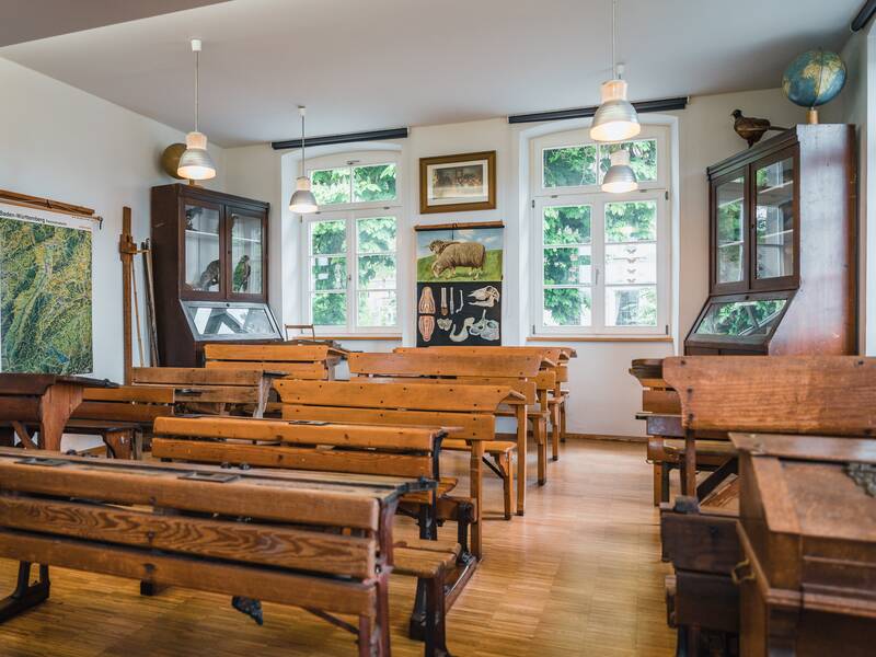 Ein klassenzimmer im altmodischen Stil mit Holzbänken, großen Fenstern, Karten und Vitrinen.
