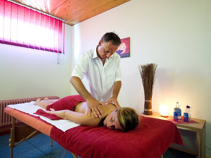 Ein Masseur massiert einer Frau im Massagezimmer des Aquaris mit gedämmtem Licht den Rücken.