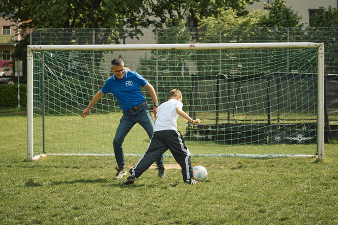 Ein Mann und ein Junge spielen auf einem Fußballfeld vor einem Tor Fußball.