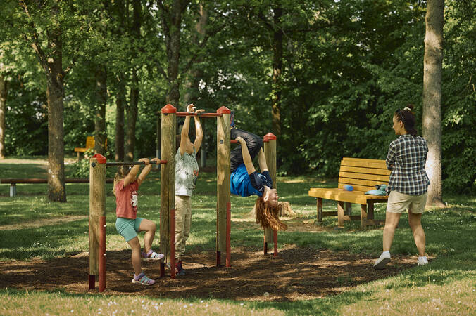 Drei Kinder spielen an Kletterstangen auf einem Spielplatz.