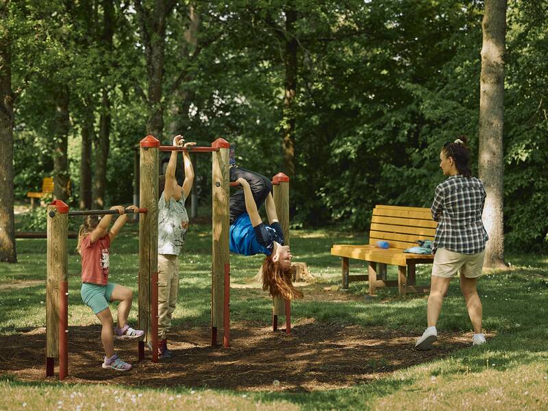 Drei Kinder spielen an Kletterstangen auf einem Spielplatz.