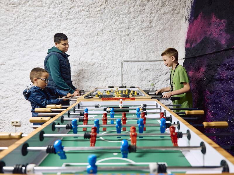 Drei Jungen stehen an dem Tischkicker im Eingangsbereich des Jugendhauses und spielen damit.