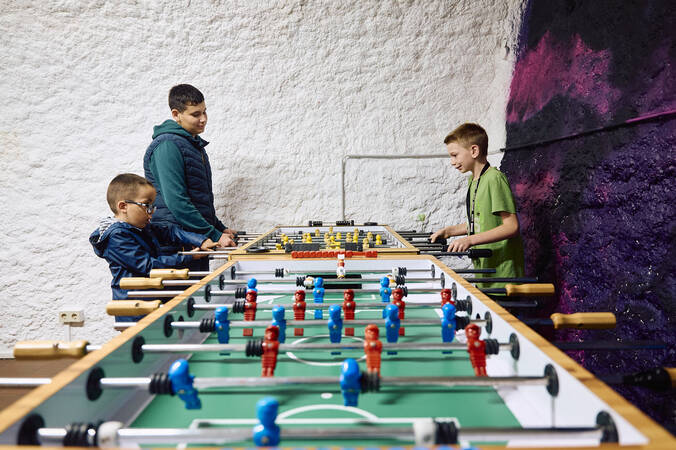 Drei Jungen stehen an dem Tischkicker im Eingangsbereich des Jugendhauses und spielen damit.