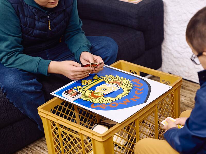Zwei Personen sitzen an einem improvisierten Tisch aus einer gelben Kiste im Jugendhaus und spielen ein Kartenspiel.