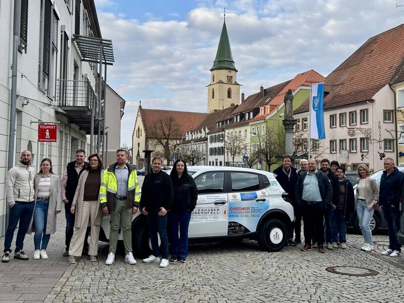 Sponsoren des neuen Elektrofahrzeuges stehen vor dem Elektrofahrzeug, das vor dem Rathaus geparkt ist.