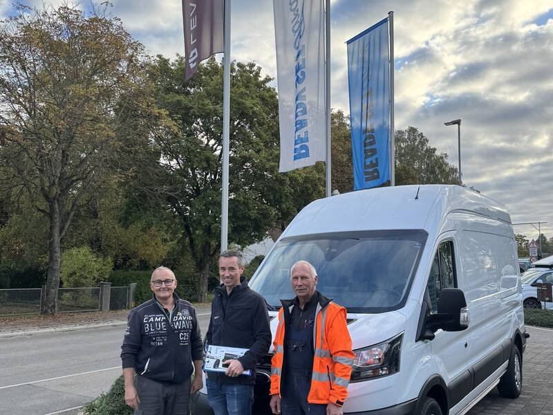 Drei Männer stehen vor dem neuen weißen Transporter für den Bauhof der Stadt Hüfingen, hinter dem sich drei Fahnenmasten mit wehenden Fahnen befinden.