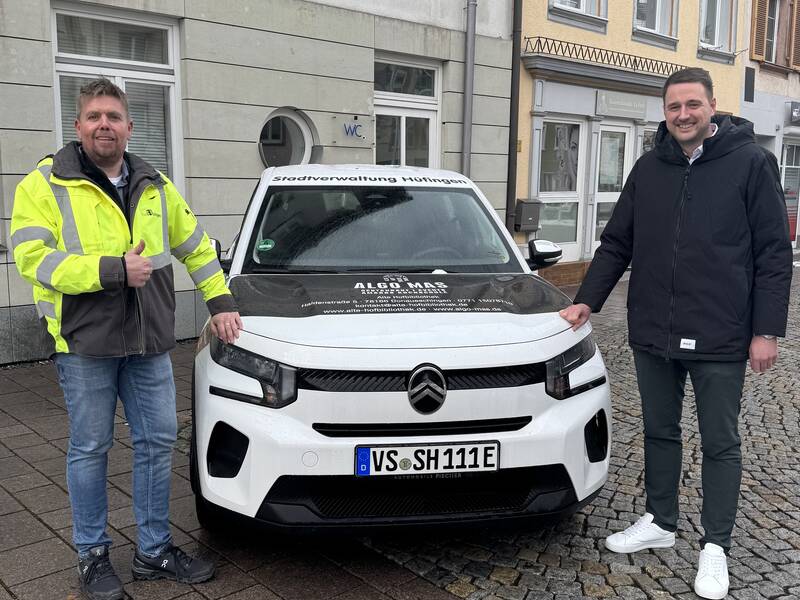 Bauamtsleiter Thilo Mayer und Bürgermeister Patrick Haas stehen neben dem neuen städtischen Elektrofahrzeug, das mit den Logos der Sponsoren beklebt ist.
