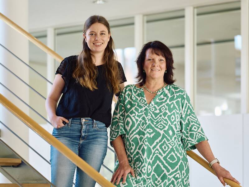 Die Mitarbeiterinnen des Amtes für Tourimus und Kultur, Frau Sarah Schindler und Frau Heidi Mayer-Löhr (von links nach rechts), stehen lächelnd auf der Treppe des modernen Rathausgebäudes nebeneinander.