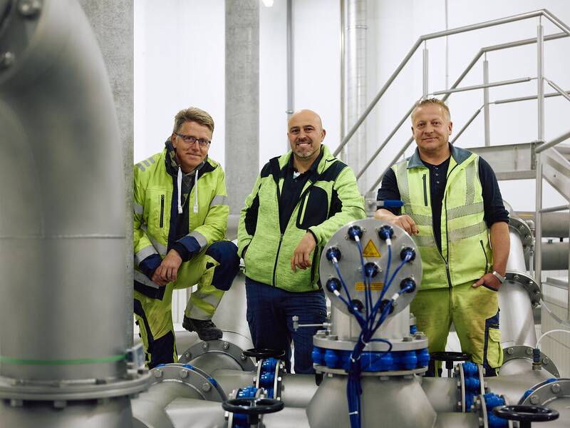 Die Mitarbeiter des Wasserwerkes stehen lächelnd zwischen Wasserrohren.