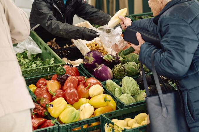 Eine Person auf einem Marktstand des Hüfinger Wochenmarktes greift nach frischem Gemüse wie Paprika, Auberginen und Artischocken.